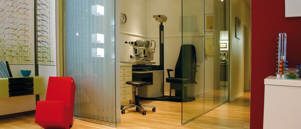 Modernes Optiker-Geschäft mit Brillengestellen, Sehtestgerät und Wartebereich.